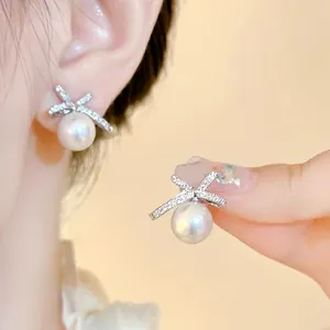 Close-up view of elegant bow pearl earrings featuring shimmering zirconia on a model.
