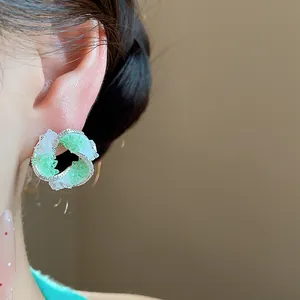 Macro close-up view of elegant green and clear glass swirl stud earrings accented with zircon