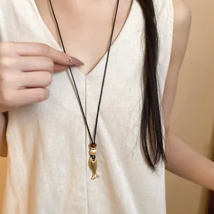 Dettaglio di una collana in pelle minimalista con ciondolo a pesce in oro opaco