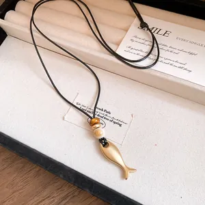 Dettaglio del ciondolo a forma di pesce dorato su una collana in cordoncino di cuoio nero.