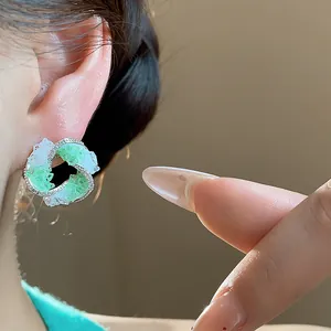 Macro detail showing green and white glass swirl stud earring with zircon on ear.