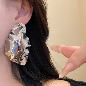 Close-up detail of geometric wrinkled silver earrings worn on ear, showing metallic texture