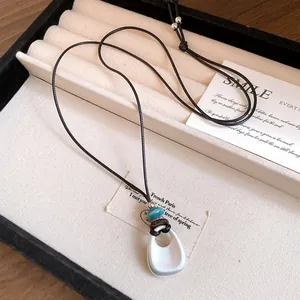 Dettaglio macro di una collana con ciondolo in ceramica minimalista e cordino in pelle nera