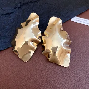 Macro detail of high-shine gold geometric pleated stud earrings with a wavy metallic texture