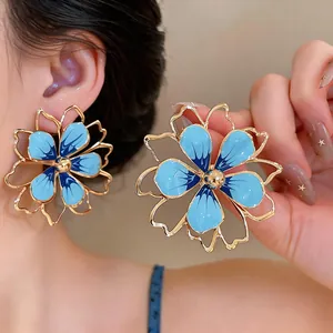 Dettaglio di orecchini a fiore in smalto blu con petali cavi dorati indosso al modello.