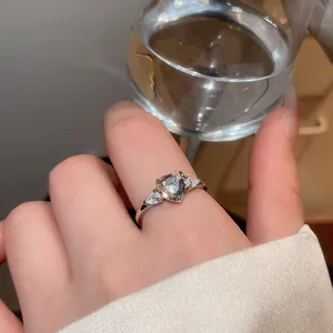Close-up of elegant silver heart-shaped zircon ring on finger with water glass background