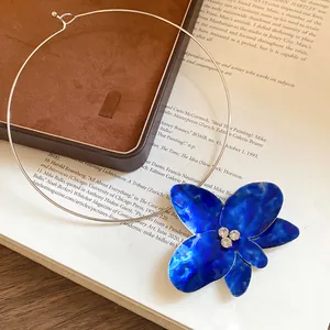 Dettaglio di un ciondolo a fiore in smalto blu vibrante su un girocollo argentato.