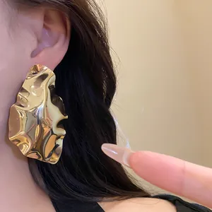 Close-up detail of a large gold-toned geometric ruffled statement earring worn on an ear.