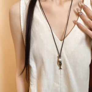 Dettaglio ravvicinato di una collana minimalista con ciondolo a pesce in ceramica retrò.