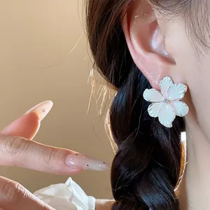 Elegante Nahaufnahme eines weißen Emaille-Blumenohrrings mit Zirkonia-Zentrum am Ohr