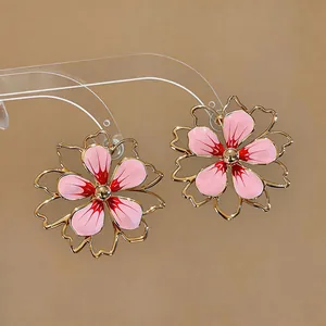 Primo piano di orecchini a lobo a fiore traforati con smalto rosa e placcatura oro