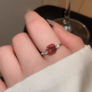 Elegant gold-tone ring featuring a vibrant cushion-cut red gemstone worn on a finger.