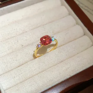Detailed shot of a gold-toned ring with a pink cushion-cut zircon in a white box.