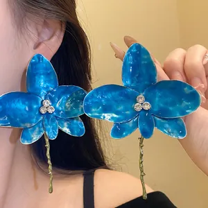 Dettaglio di orecchini a fiore in smalto blu con centro di strass brillante su modella