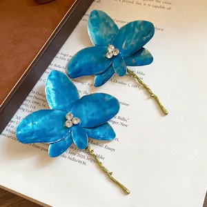 Primo piano di orecchini a fiore in smalto blu con strass scintillanti e steli verdi