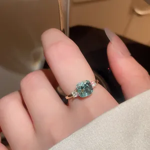 Detailed view of a vintage gold ring with a sparkling teal cushion-cut zircon on a finger.
