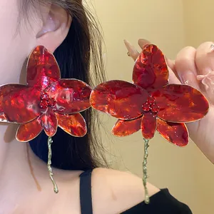 Dettaglio ravvicinato di grandi orecchini a orchidea in smalto rosso con strass chic