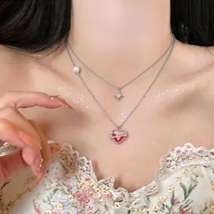 Close-up of double-layer silver heart necklace with red enamel and zircon star detail.