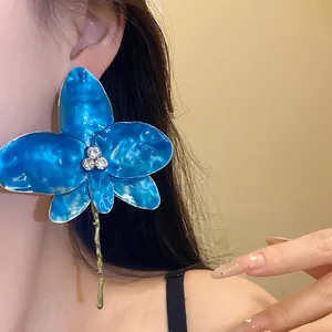 Dettaglio di grandi orecchini a fiore in smalto blu con strass scintillanti e brillanti
