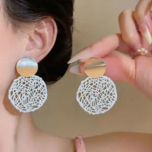 Close-up view of elegant white hollow bird nest earrings with polished gold metal discs