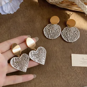 Detailed view of hollow heart and round stud earrings with a mixed metallic finish.