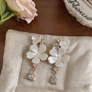 Detailed view of white flower earrings with sparkling zircon teardrop pendants.