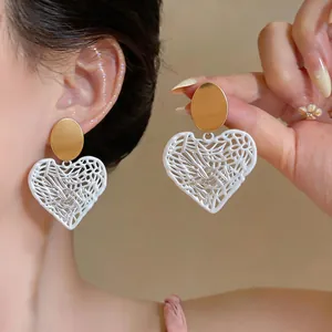 Detailed view of white filigree heart earrings with golden studs worn by a model