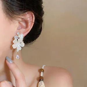 Close-up of elegant gold-plated floral stud earrings with teardrop zircon on model's ear