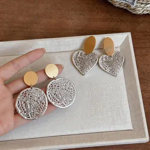 Close-up detail of silver hollow heart and round filigree earrings with gold studs