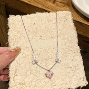 Close-up of a silver-tone necklace featuring a pink enamel heart and pearl accents.