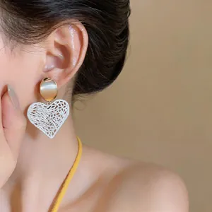 Elegant white hollow heart dangle earrings with gold stud shown on model for a chic look