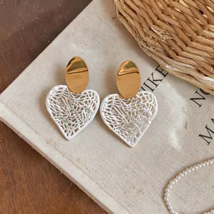 Close-up detail of hollowed-out heart earrings with gold studs and white lace texture
