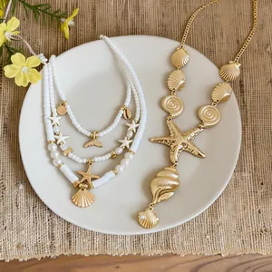 Detail view of gold seashell and starfish necklaces styled on a white plate for vacation