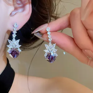 Close-up of sparkling geometric rhombus earrings with marquise zircon leaves and purple stones