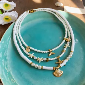 Detailed view of white multi-strand beach necklace with gold starfish and seashell charms on plate.