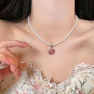 Close-up view of an elegant red enamel heart pendant on a delicate white pearl necklace