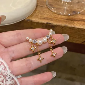 Detail view of gold-plated earrings with white pearls, zircons, and dangling star charms