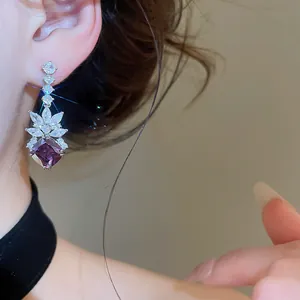 Close-up of elegant purple diamond-shaped zircon pendant earrings on model