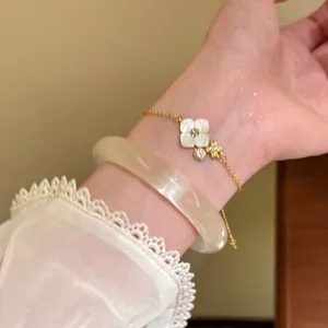 Close-up of elegant gold flower bracelet and white bangle on woman's wrist