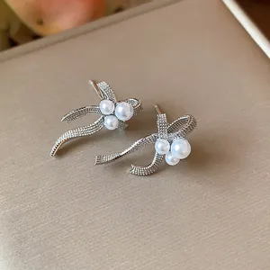 Detailed view of silver-tone bow earrings featuring three white pearls on a tan backdrop.