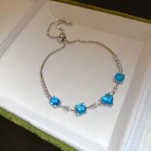 Détail d'un bracelet en chaîne argentée orné de zircons bleus en forme de cœur étincelants.