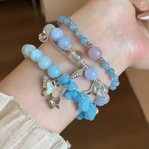 Détail de bracelets superposés en aigue-marine bleue avec breloque papillon