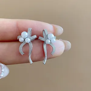 Detailed macro shot of silver bow-shaped stud earrings with delicate pearls held by hand