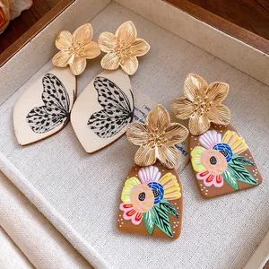 Close-up of golden metal flower earrings with butterfly and floral acetate pendants