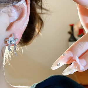 Close-up view of elegant bow-shaped pearl earrings on a model's ear with warm lighting.