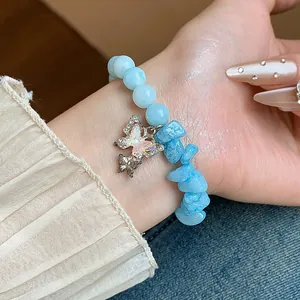 Gros plan d'un bracelet en aigue-marine naturelle avec une pierre et un charme de papillon.