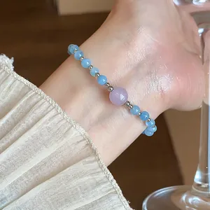 Gros plan d'un bracelet en perles d'aigue-marine et lavande sur un poignet avec manche plissée.