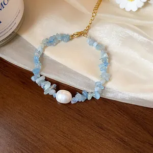 Gros plan de pierres d'aigue-marine irrégulières et perle sur un bracelet chaîne en or.