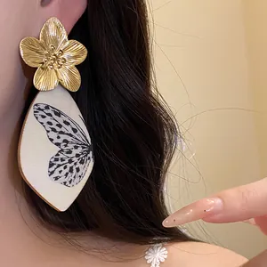 Detailed macro view of golden metal flower earrings with butterfly acetate pendant