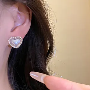 Elegante pendiente de perla con forma de corazón y borde de cristal en la oreja de modelo.